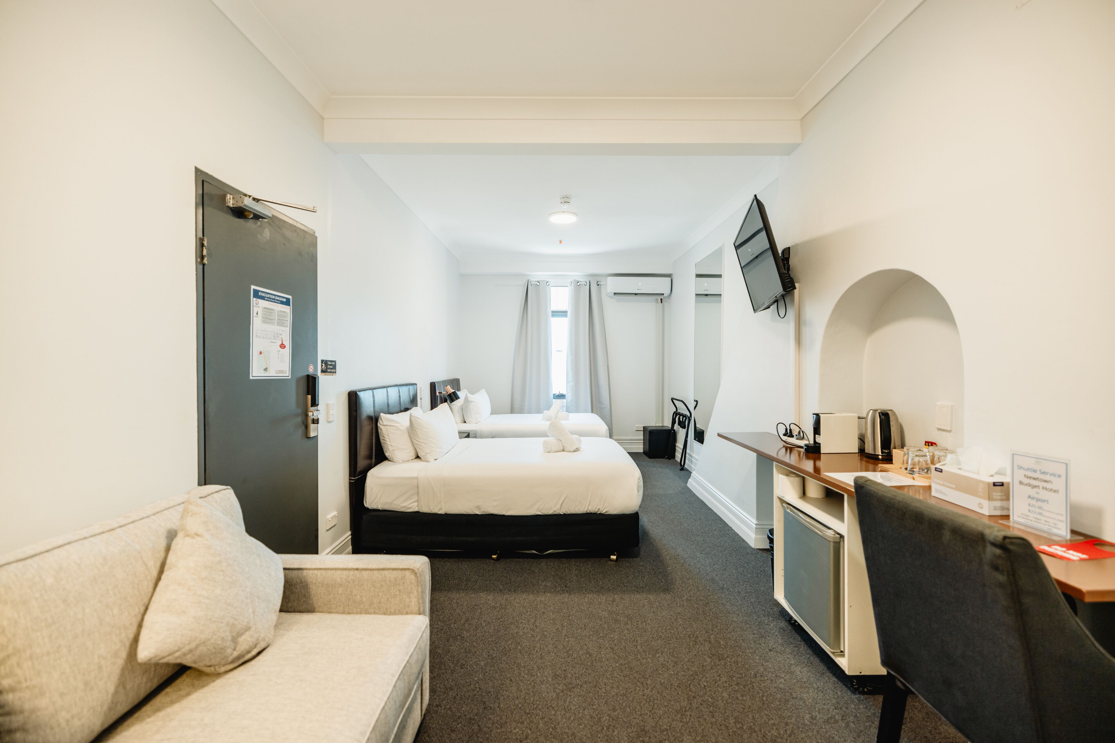 A hotel room with a bed, a desk, a chair, a sofa, and a TV mounted on the wall.