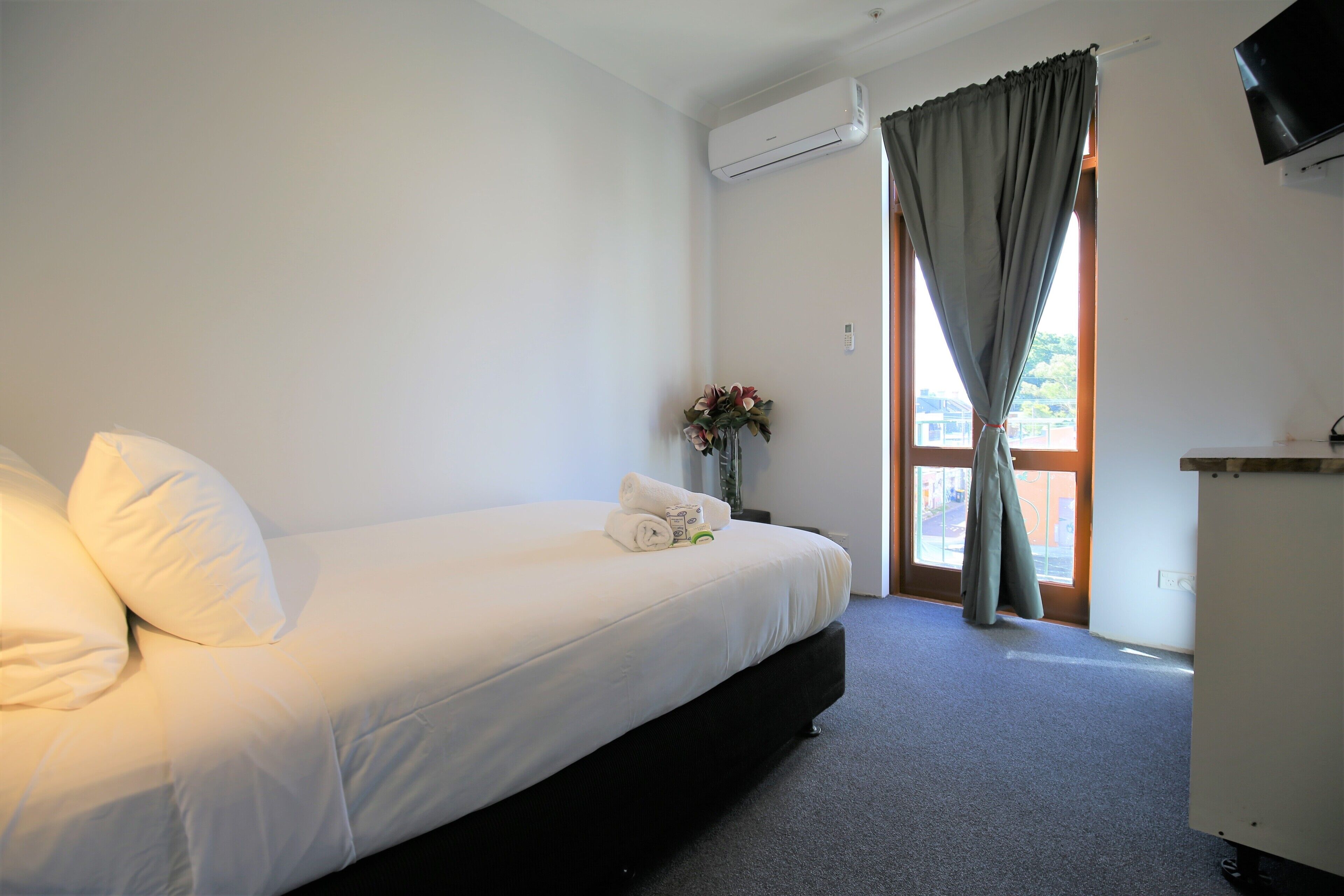 A hotel room with a bed, a desk, and a window with curtains.