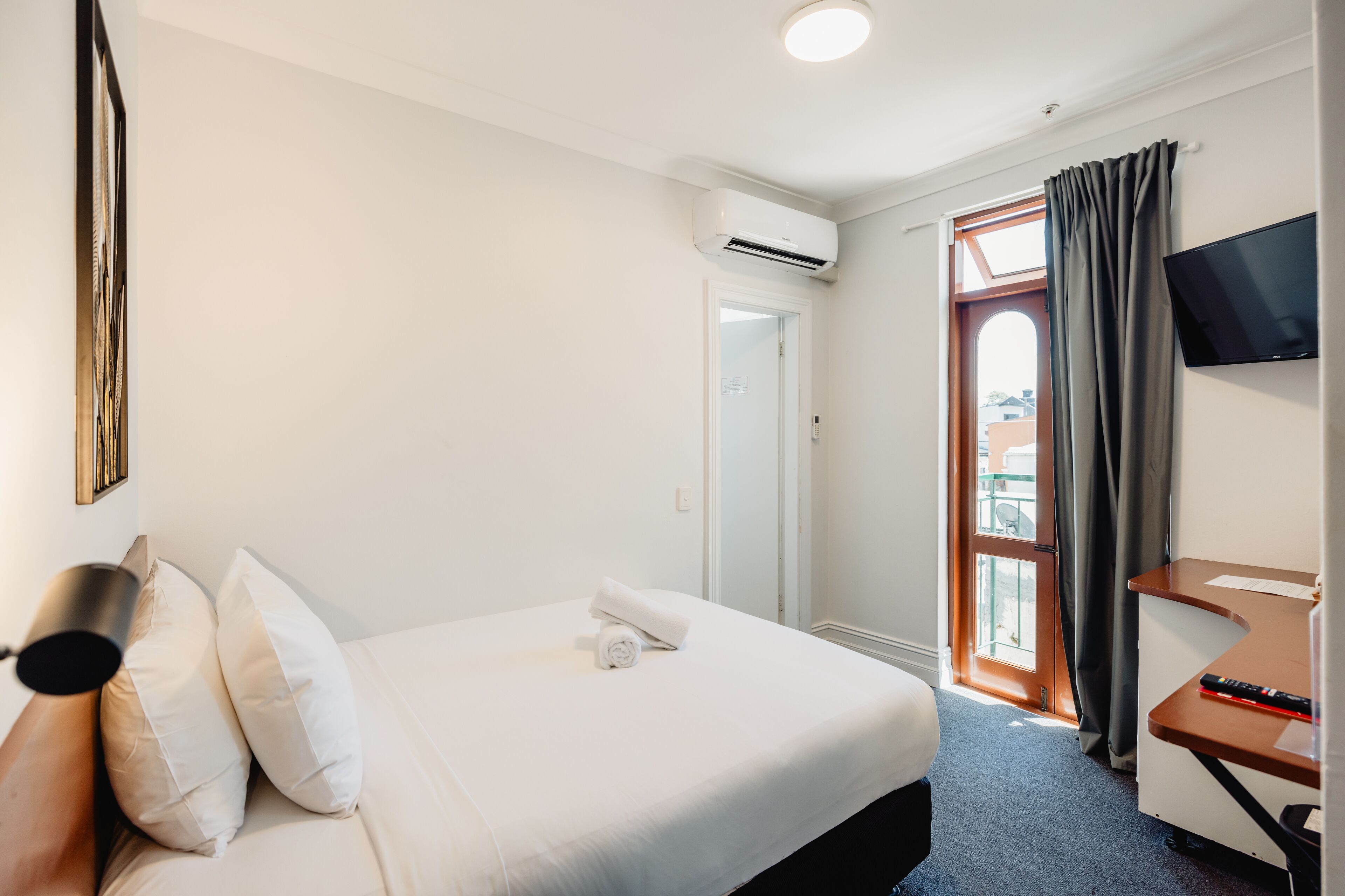 A hotel room with a bed, a desk, a TV, and a window with curtains.