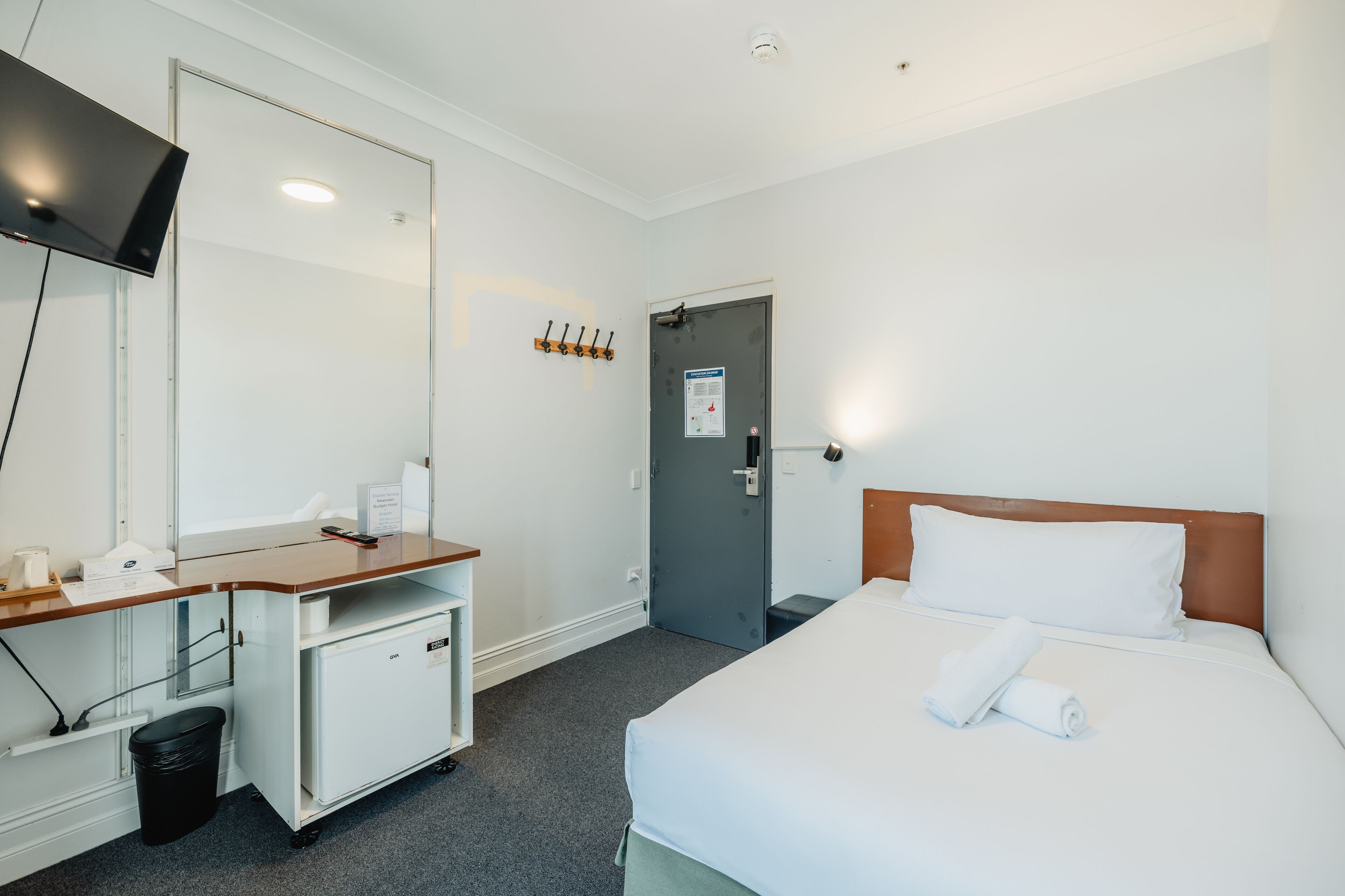 Une chambre d’hôtel avec un lit, un bureau avec un ordinateur, un miroir, un porte-manteau et une porte.