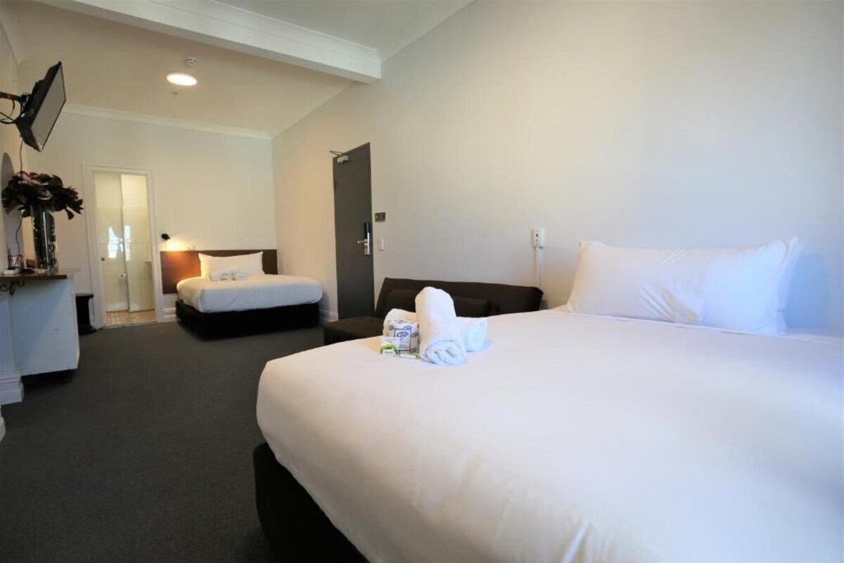 A hotel room with a large bed, a smaller bed, a desk with a lamp, and a door leading to another room.