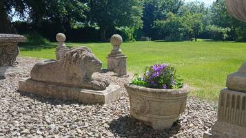 Un jardín con esculturas de piedra, incluyendo un león y una esfinge, además de una planta en maceta con flores moradas.