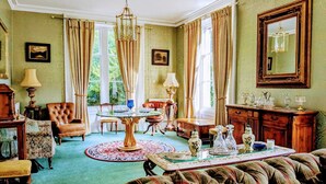 A room with a green carpet, a round table with chairs, a sofa, a cabinet, and a large mirror on the wall. - The Gables (Berwick-upon-Tweed)
