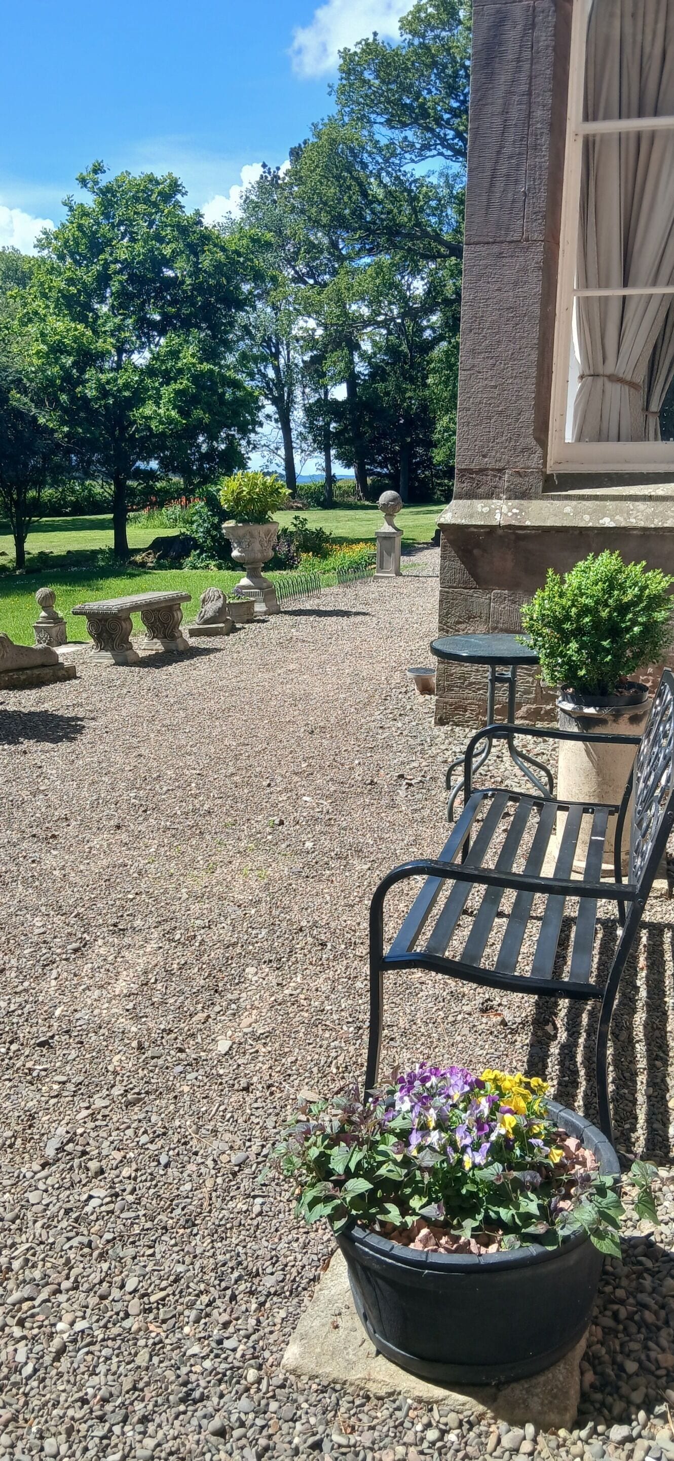 Uma área de pátio com bancos de pedra, uma mesa e plantas em vasos.