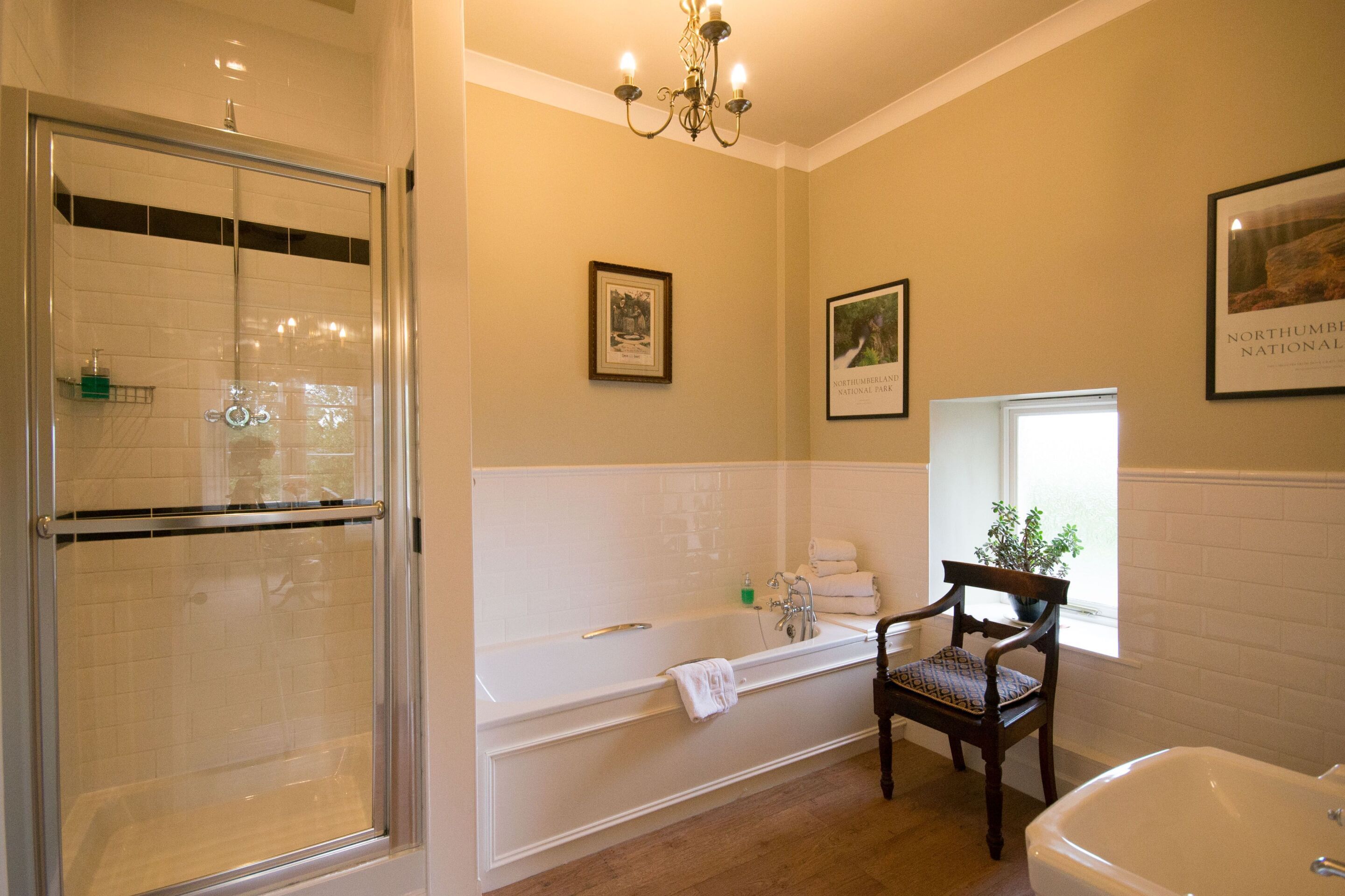 A bathroom with a glass-enclosed shower, a freestanding bathtub, a wooden chair, and a large mirror.