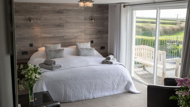 Et moderne soveværelse med en stor seng, et træhovedgærde og en balkon med udsigt over landskabet.