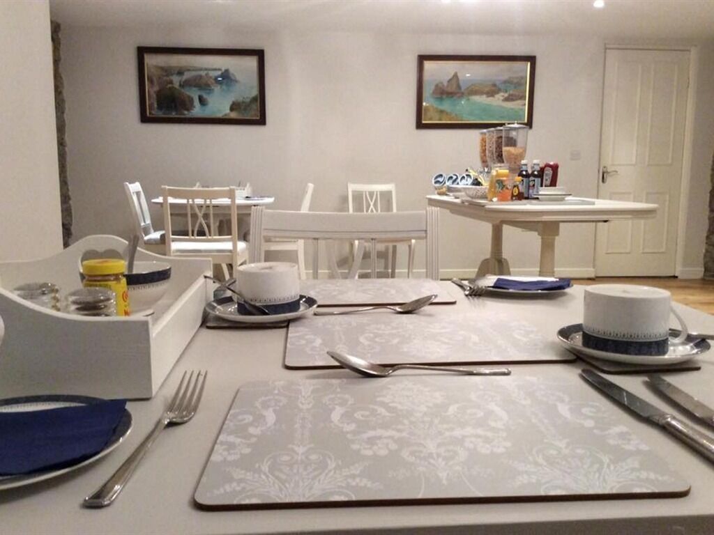 A dining area with a table set for four, including plates, cutlery, and a cup. There are chairs around the table, and a white door is visible in the background.