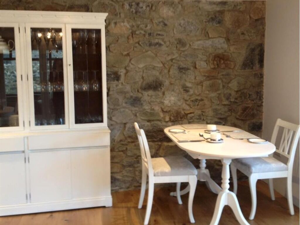 Een eetgedeelte met een ronde tafel en vier stoelen, een witte kast met glazen deuren en een stenen muur.
