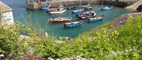 A harbor with boats docked at a stone pier, surrounded by greenery and flowers.