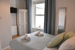 Ein Schlafzimmer mit Bett, einem Fenster mit Vorhängen, einem Heizkörper und einem Kleiderschrank.