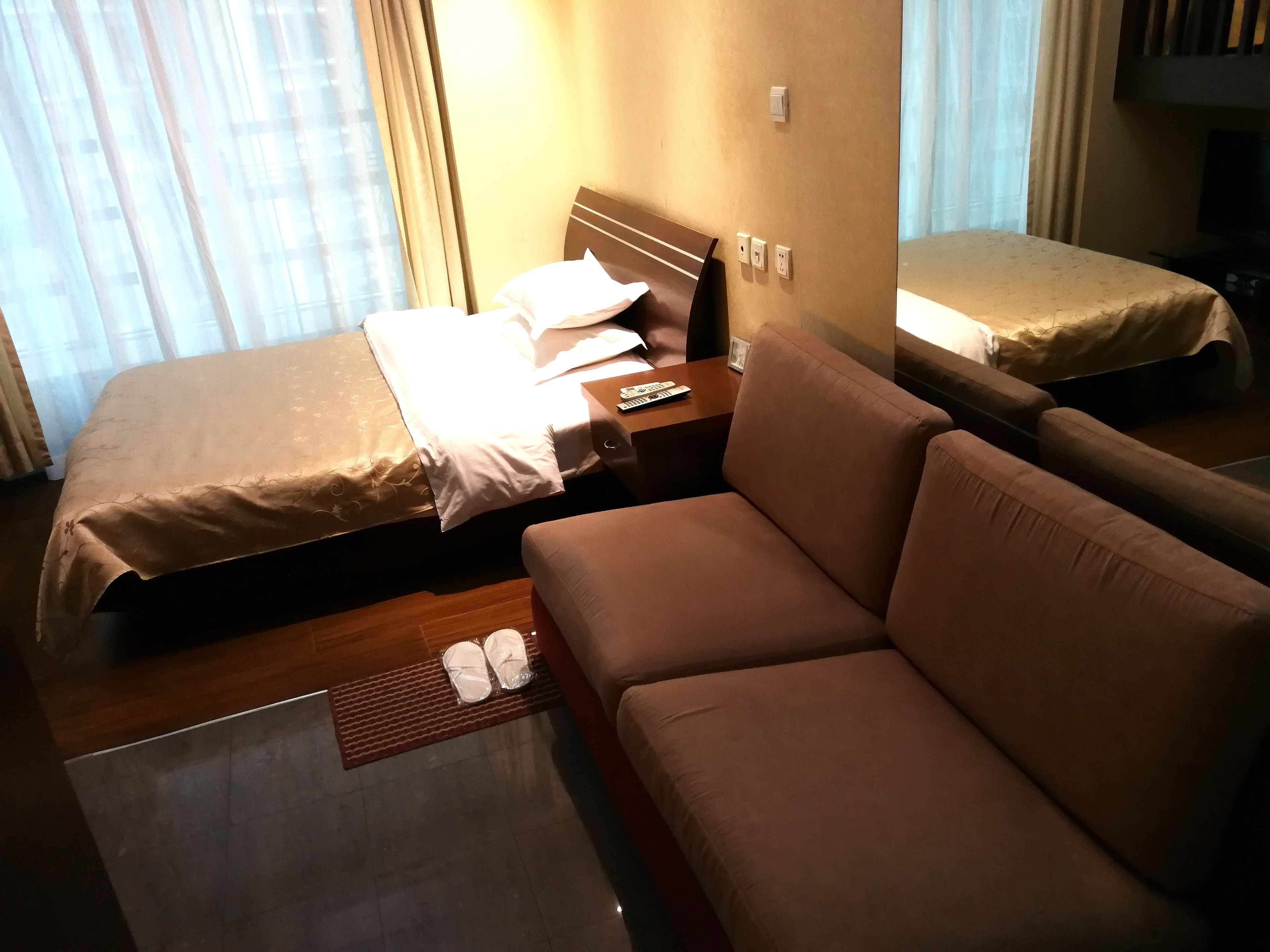 Habitación de hotel con dos camas, un sofá, una mesita de noche y un par de pantuflas sobre un tapete.