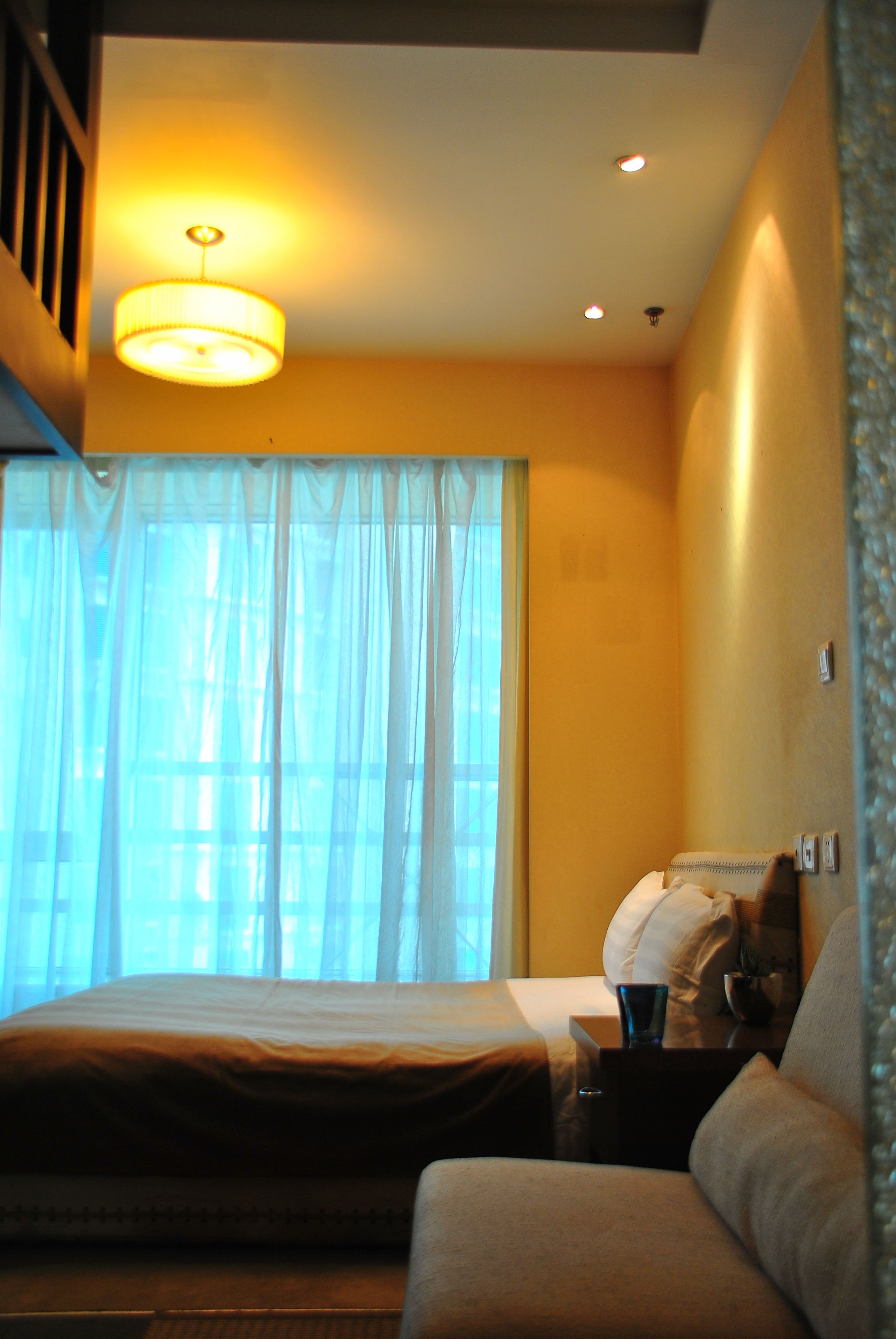 Une chambre d’hôtel avec un lit, une table de chevet, une lampe et une fenêtre avec des rideaux.