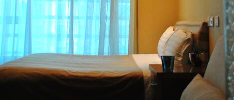 A hotel room with a bed, a nightstand, a lamp, and a window with curtains.