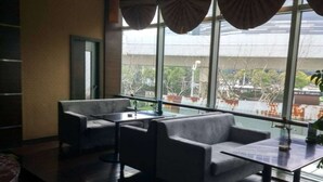 Un espace de détente moderne avec un canapé et une table, de grandes fenêtres avec des rideaux et une vue sur l’extérieur.