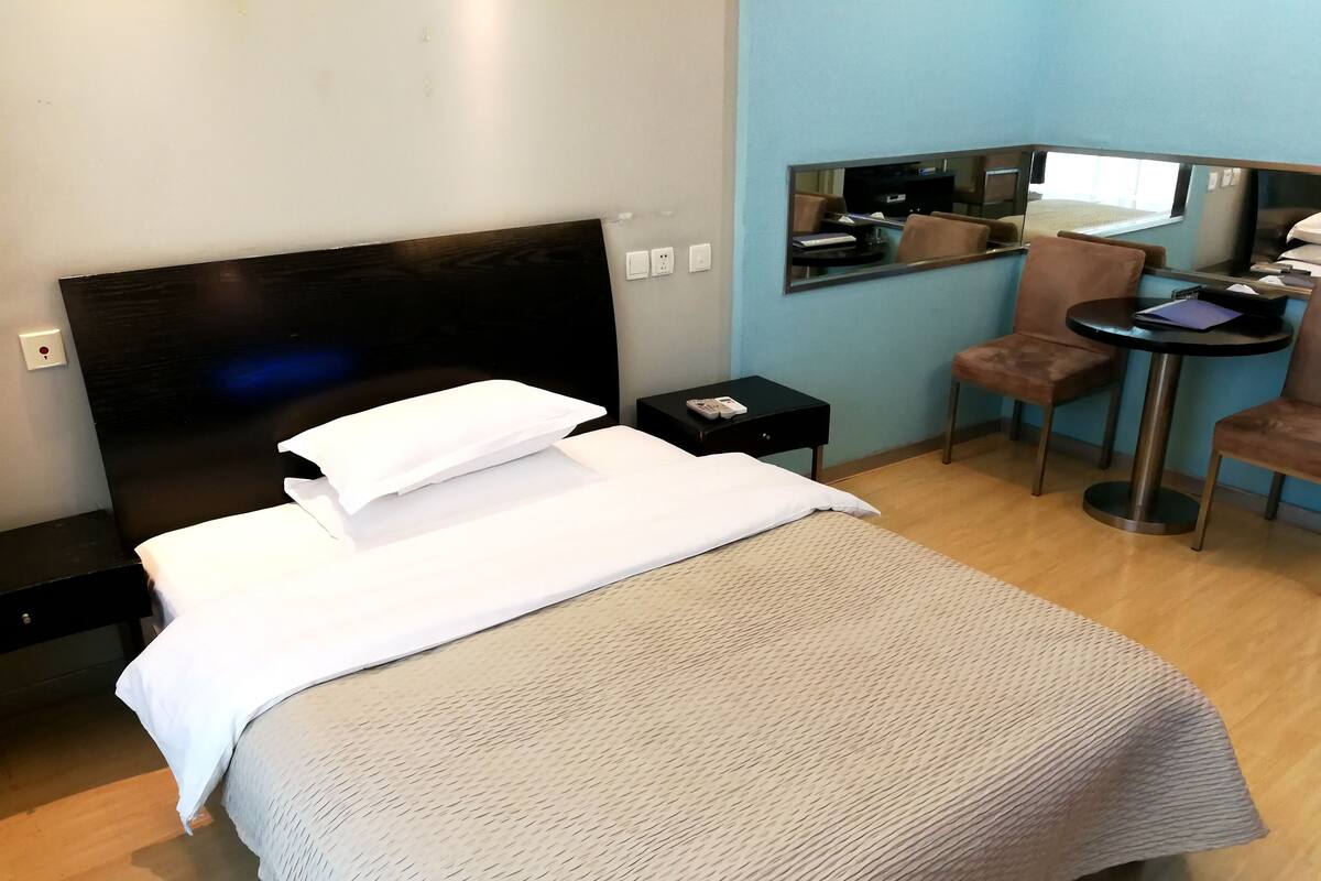 Ein Hotelzimmer mit einem Bett, einem kleinen Tisch mit Stuhl, einem Spiegel und einem Fenster.