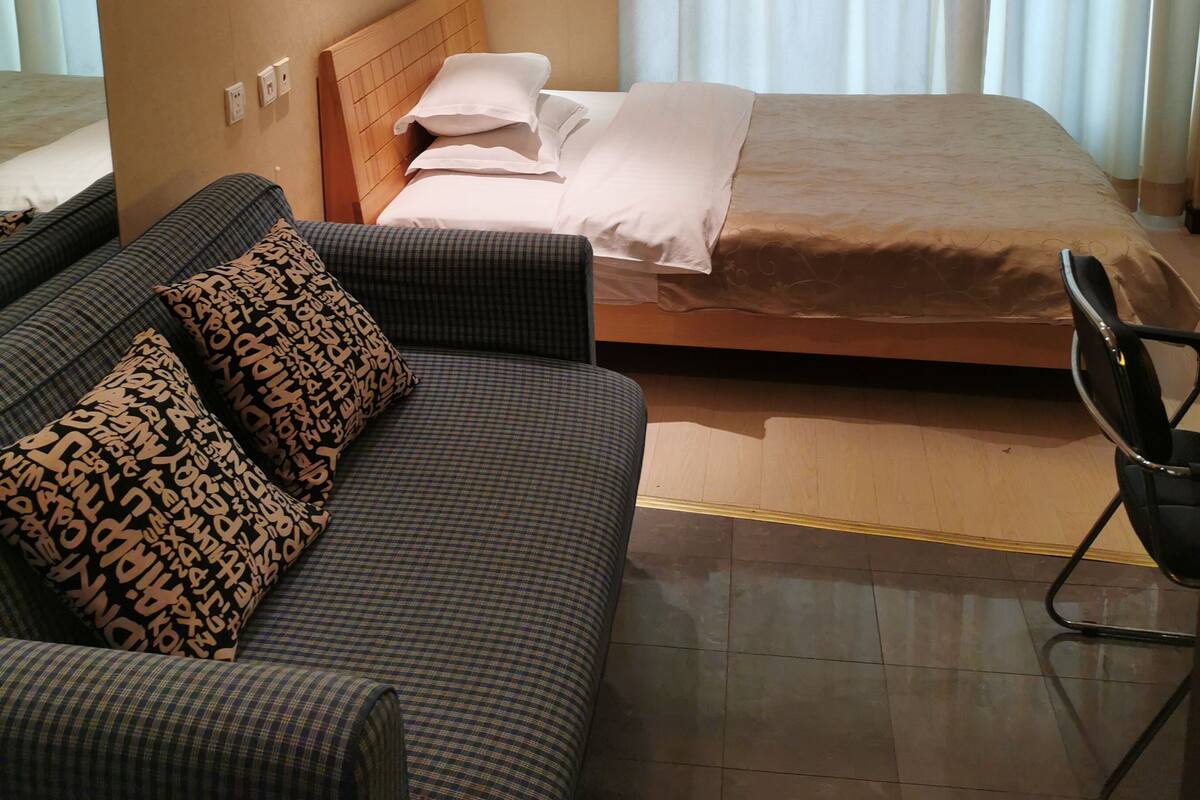 Ein Hotelzimmer mit Bett, einer Couch, einem Sessel und einem großen Fenster mit Vorhängen.