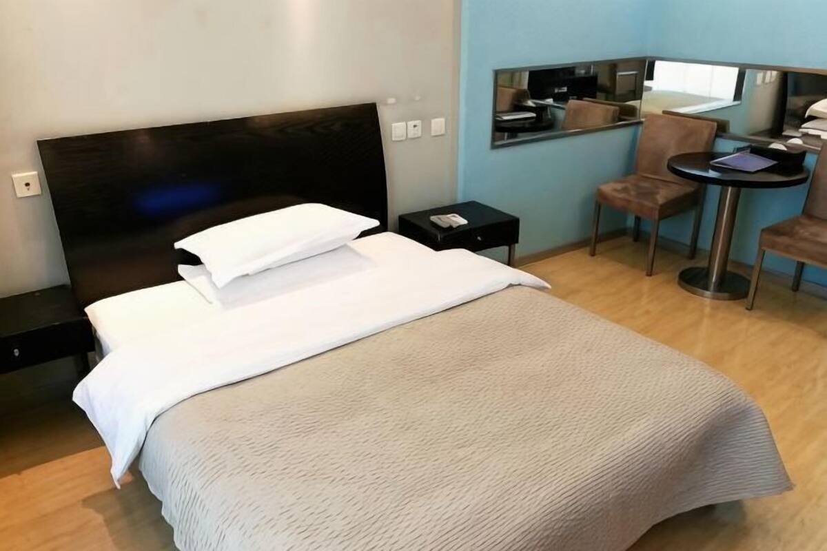 Ein Hotelzimmer mit Bett, einem kleinen Tisch, einem Sessel, einem Schreibtisch und einem Spiegel.