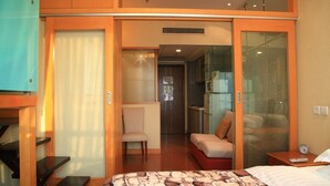 Une chambre d’hôtel comprenant un lit, une chaise, une petite table et une porte coulissante donnant accès à la salle de bain.