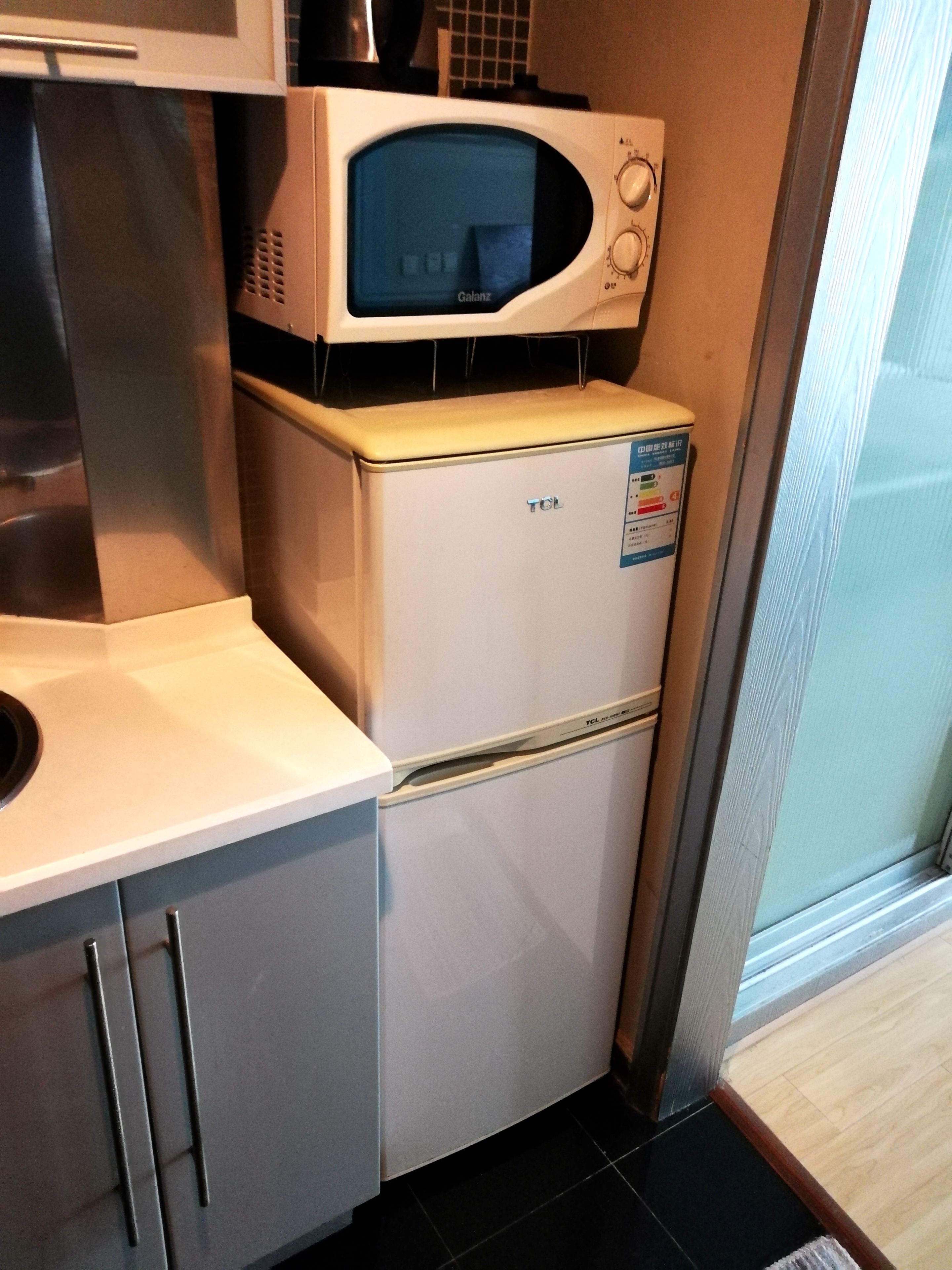 A compact kitchen with a microwave on top of a refrigerator, a sink, and cabinets.