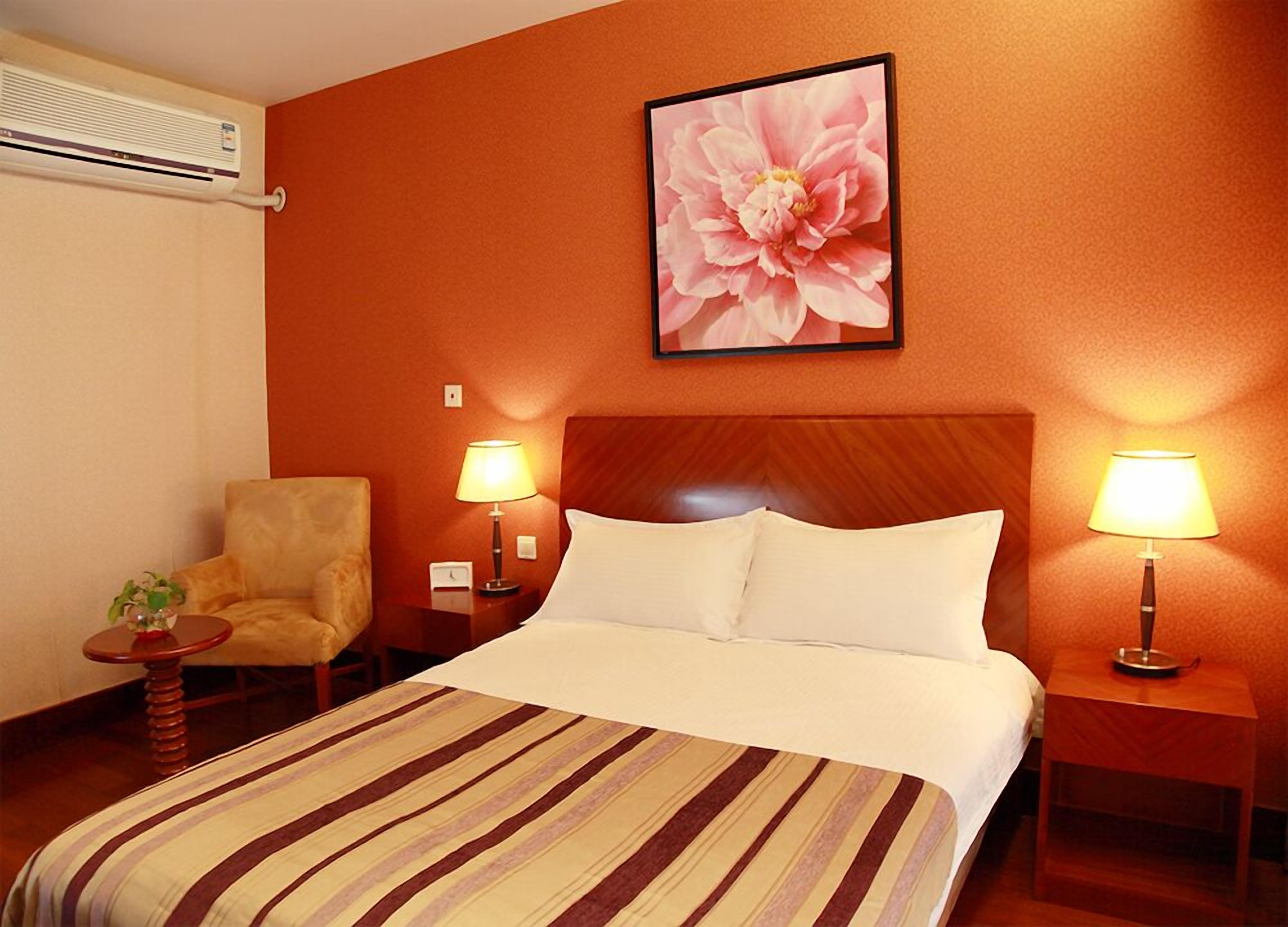 Una habitación de hotel con una cama grande, dos lámparas de noche, una silla y un aire acondicionado instalado en la pared.