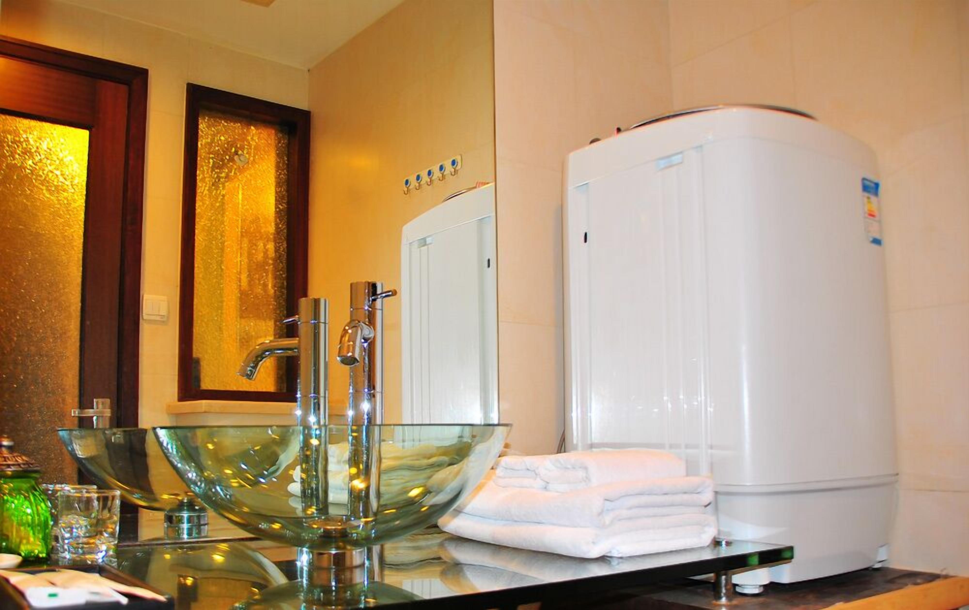 Un baño con un lavabo de cristal, un toallero blanco y un calentador de agua blanco.