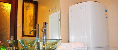 Un baño con un lavabo de cristal, un toallero blanco y un calentador de agua blanco.