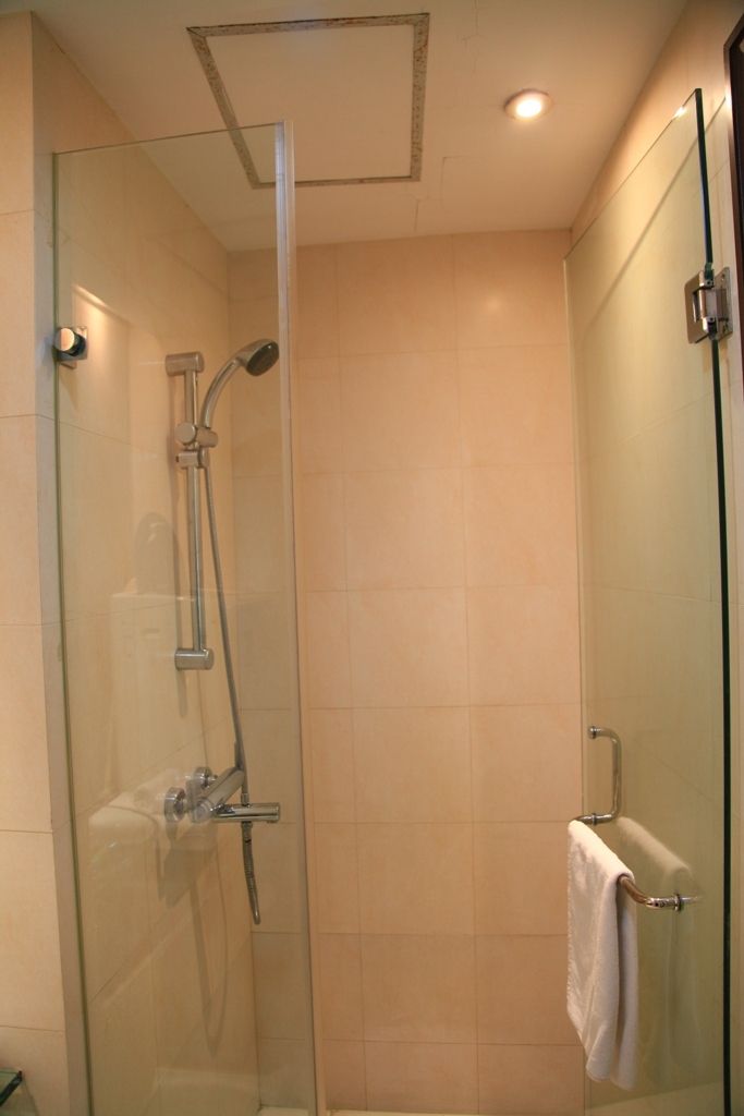 A glass-enclosed shower with a handheld showerhead and a wall-mounted faucet.