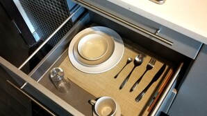 Une cuisine équipée d’une cuisinière, d’un tiroir contenant une batterie de cuisine, des ustensiles et un verre.