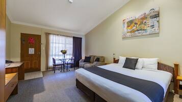 A hotel room with a large bed, a desk, a chair, a small table, and a painting on the wall.