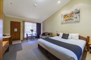 A hotel room with a large bed, a desk, a chair, a small table, and a painting on the wall.