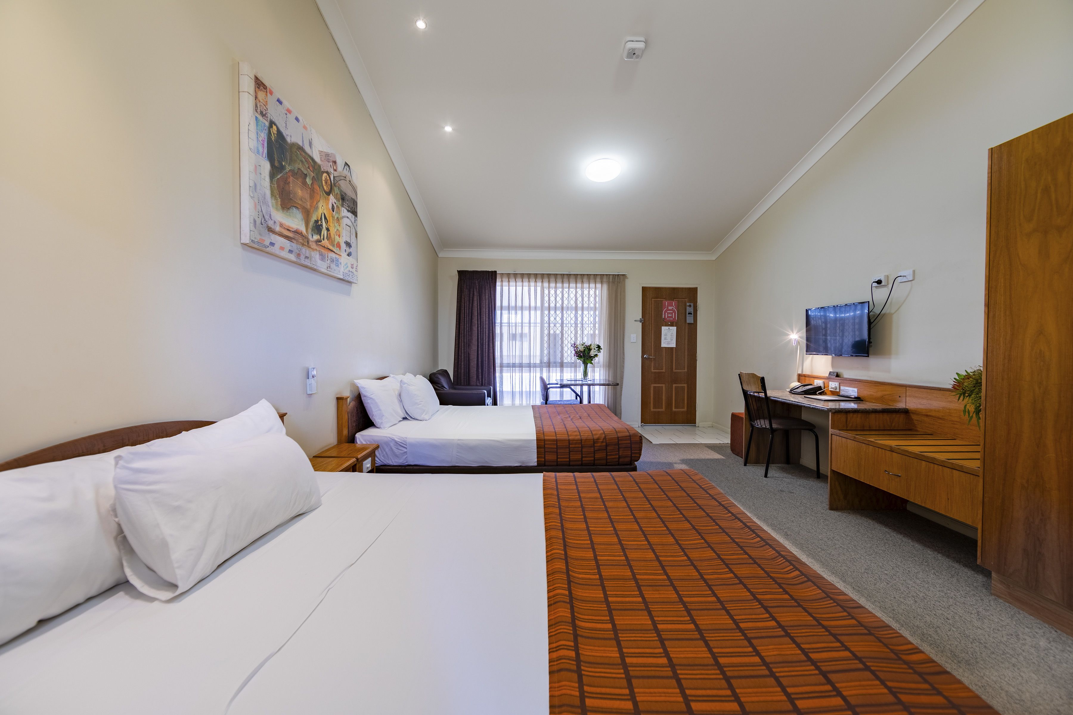 A hotel room with two beds, a desk, a chair, a television, and a window with curtains.
