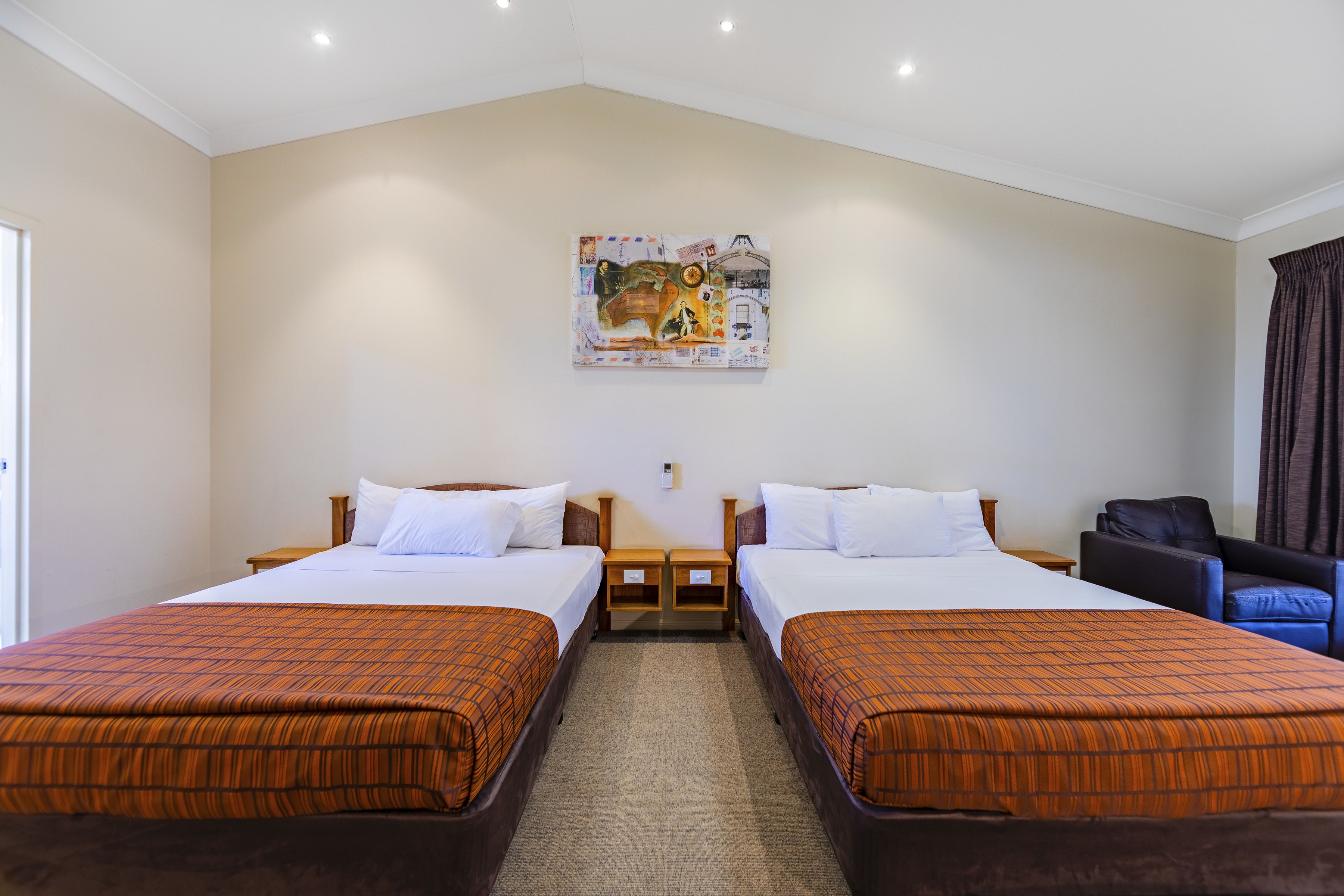 A hotel room with two beds, a painting on the wall, a chair, and a window.