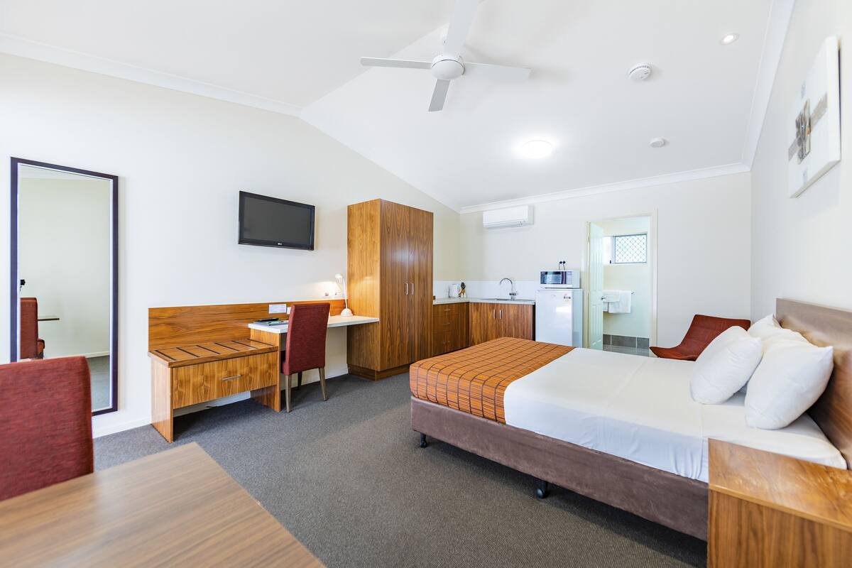 A hotel room with a bed, desk, chair, wardrobe, and a television.