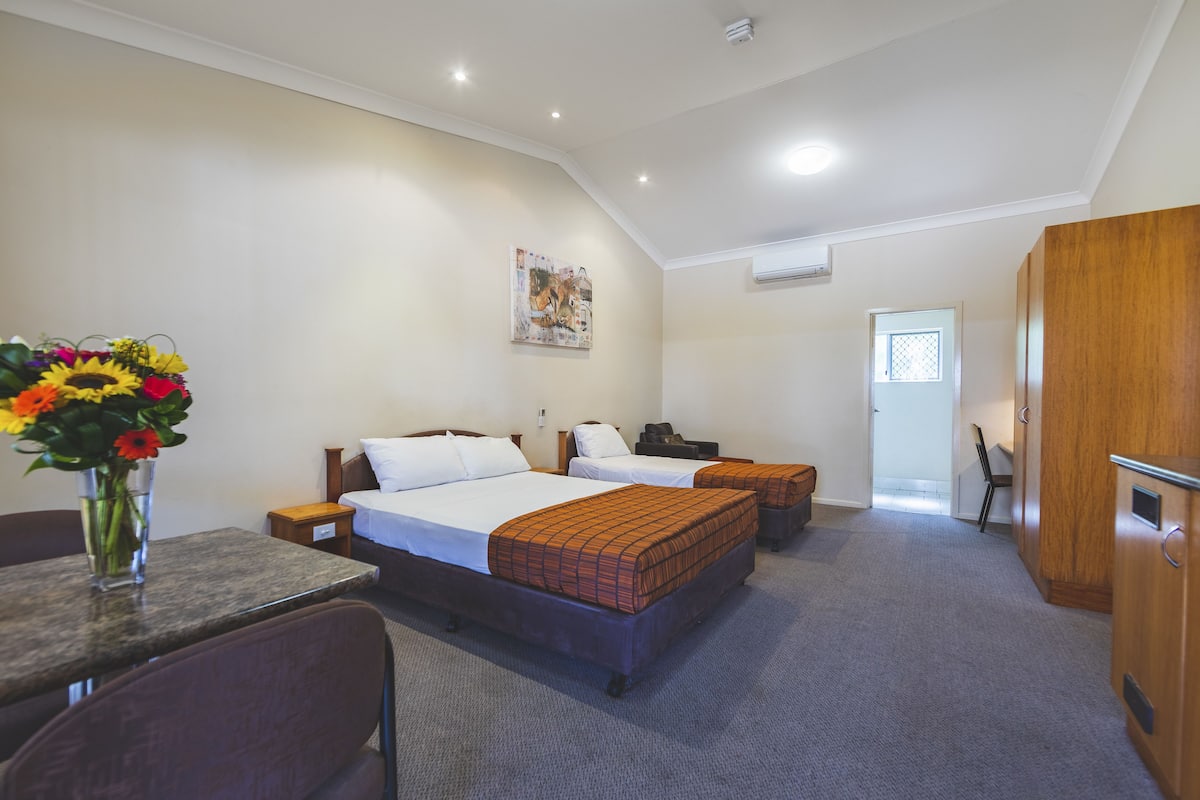 A hotel room with two beds, a desk, a chair, a wooden wardrobe, and a painting on the wall.