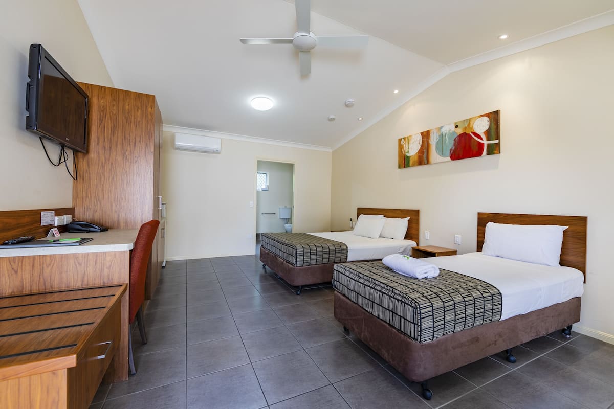 A hotel room with a desk, two beds, a ceiling fan, and artwork on the wall.