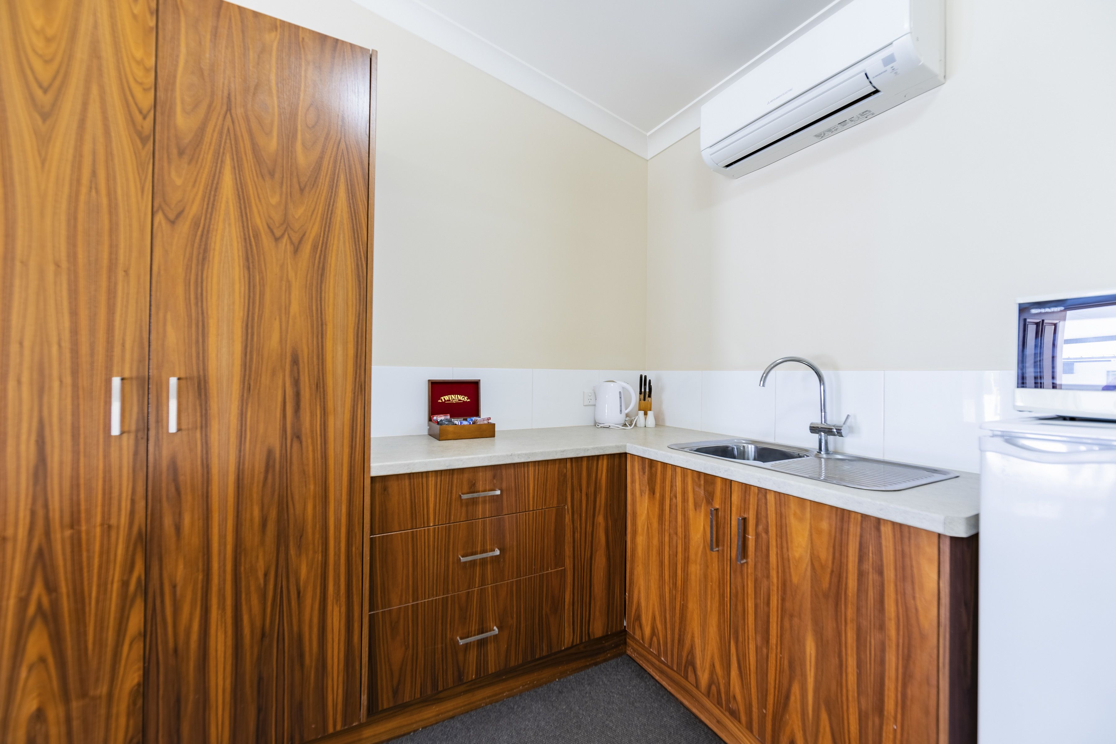 Una cocina moderna con armarios de madera, encimera blanca, un lavabo y un aire acondicionado.