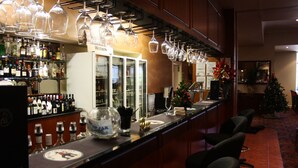 Zona de bar con estantes llenos de botellas de licor, un enfriador de vinos y copas de vino colgantes.