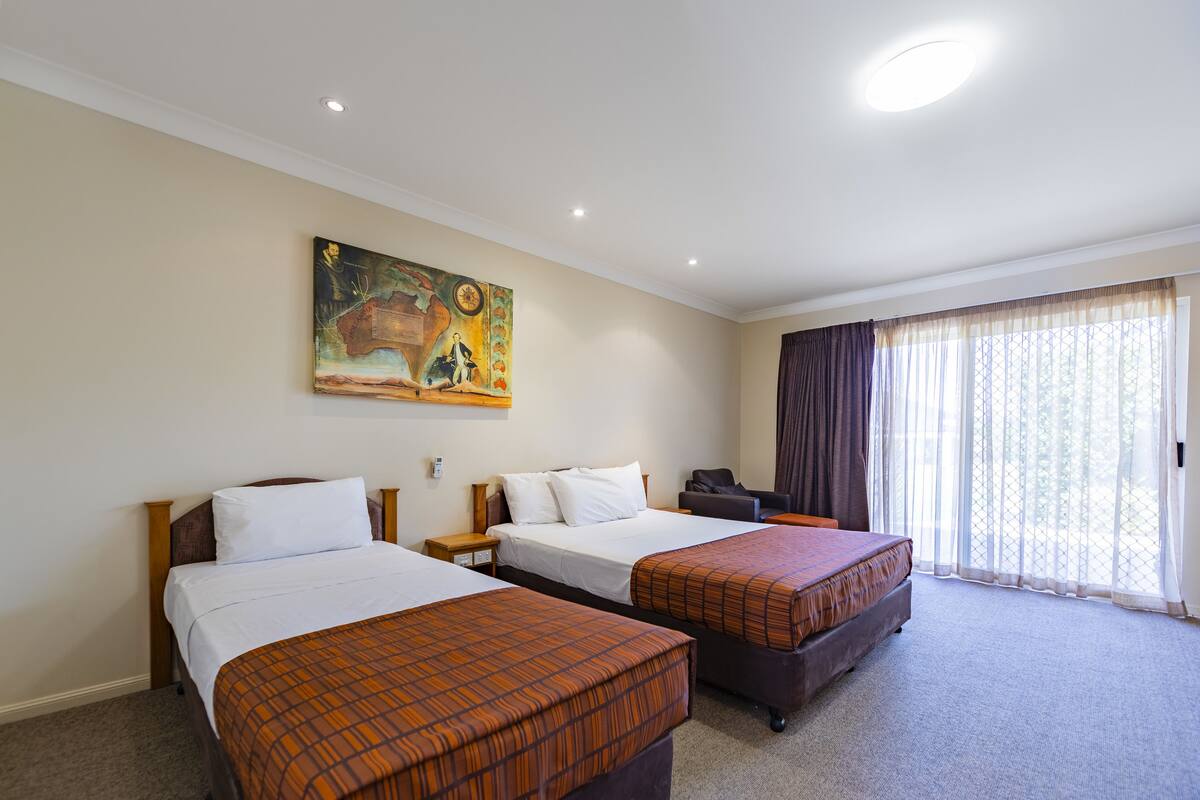 A hotel room with two beds, a painting on the wall, a desk, and a large window with curtains.