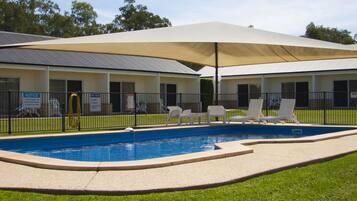 A swimming pool with lounge chairs and a canopy, surrounded by a fence and a building with multiple doors.