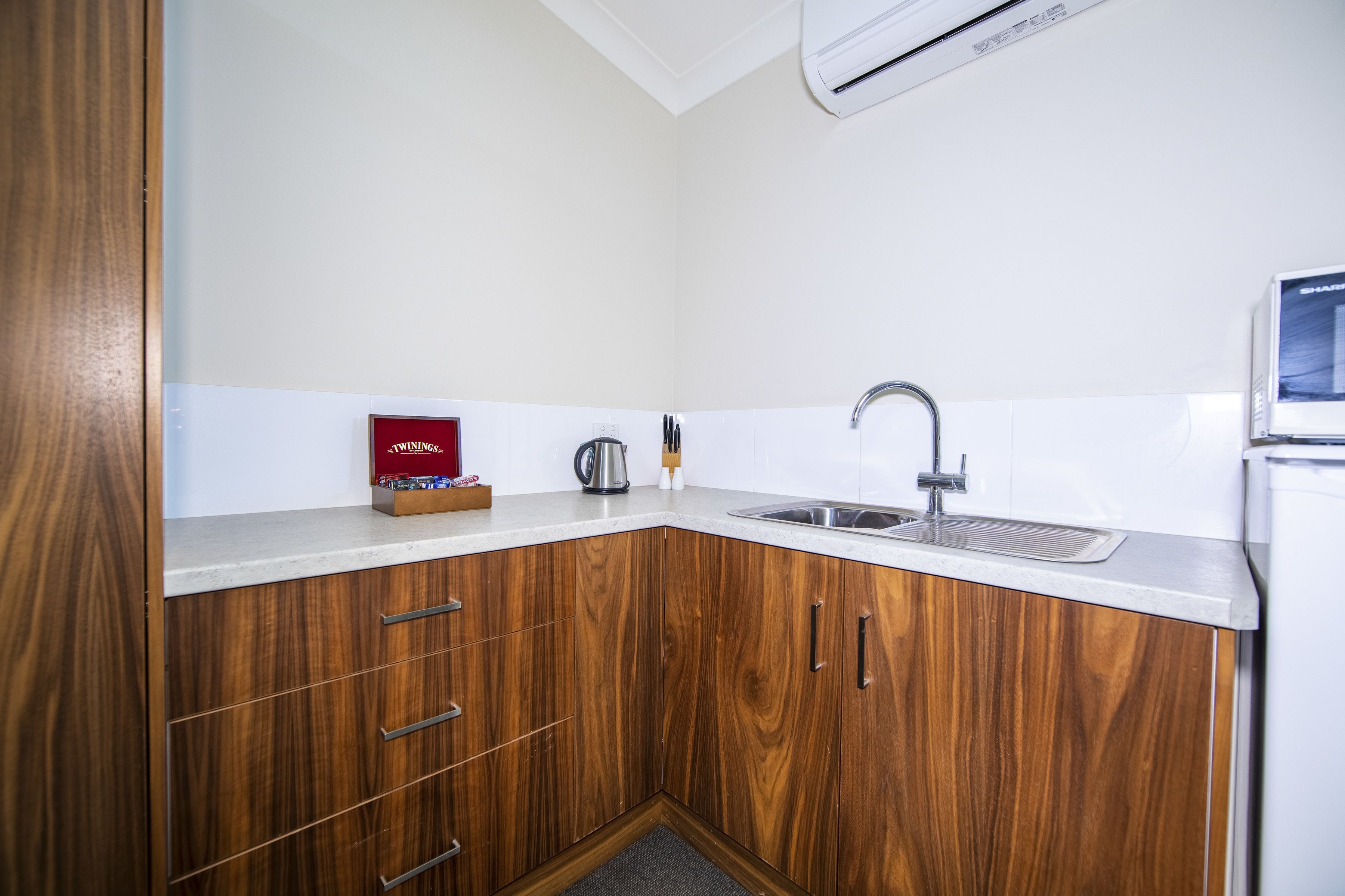 A compact kitchen with wooden cabinets, a stainless steel sink, and a built-in microwave.
