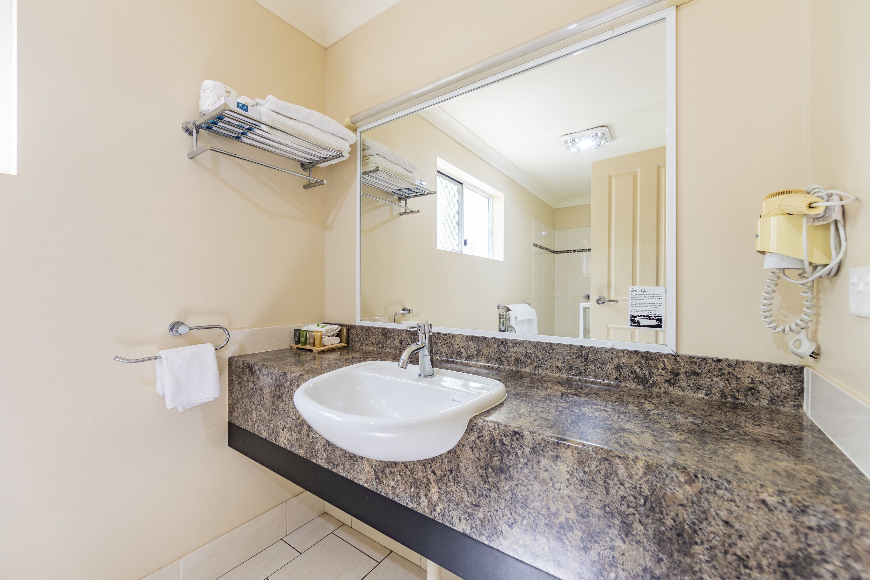 A bathroom with a granite countertop, a white sink, a towel rack, a mirror, and a hairdryer on the wall.