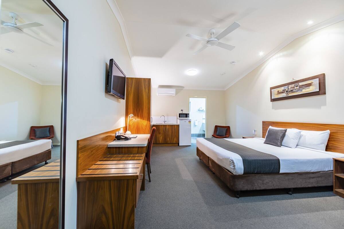 A hotel room with a bed, desk, chair, and a kitchenette area.