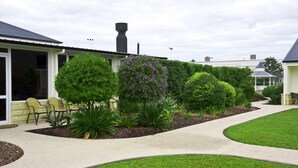 Una propiedad residencial con jardín ajardinado, terraza techada y chimenea.