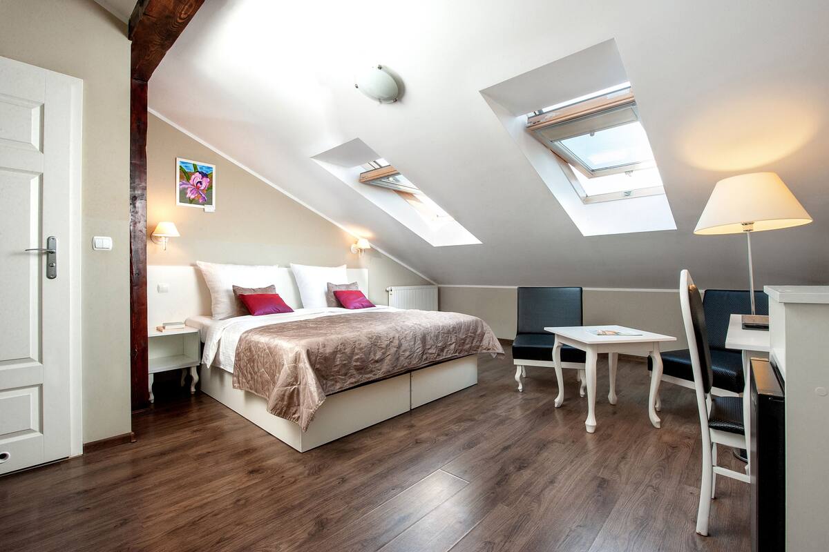 A bedroom with a bed, bedside tables, a desk, and a chair. There are skylights on the ceiling.