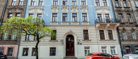 Un edificio de varios pisos con una entrada central, ventanas amplias y un árbol en frente.