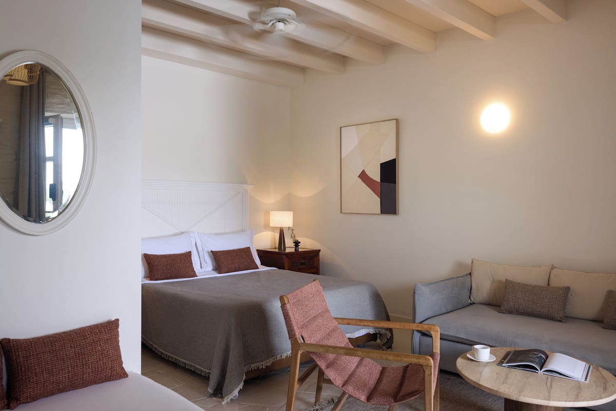 Un dormitorio con cama, sofá, sillón, mesa y lámpara.
