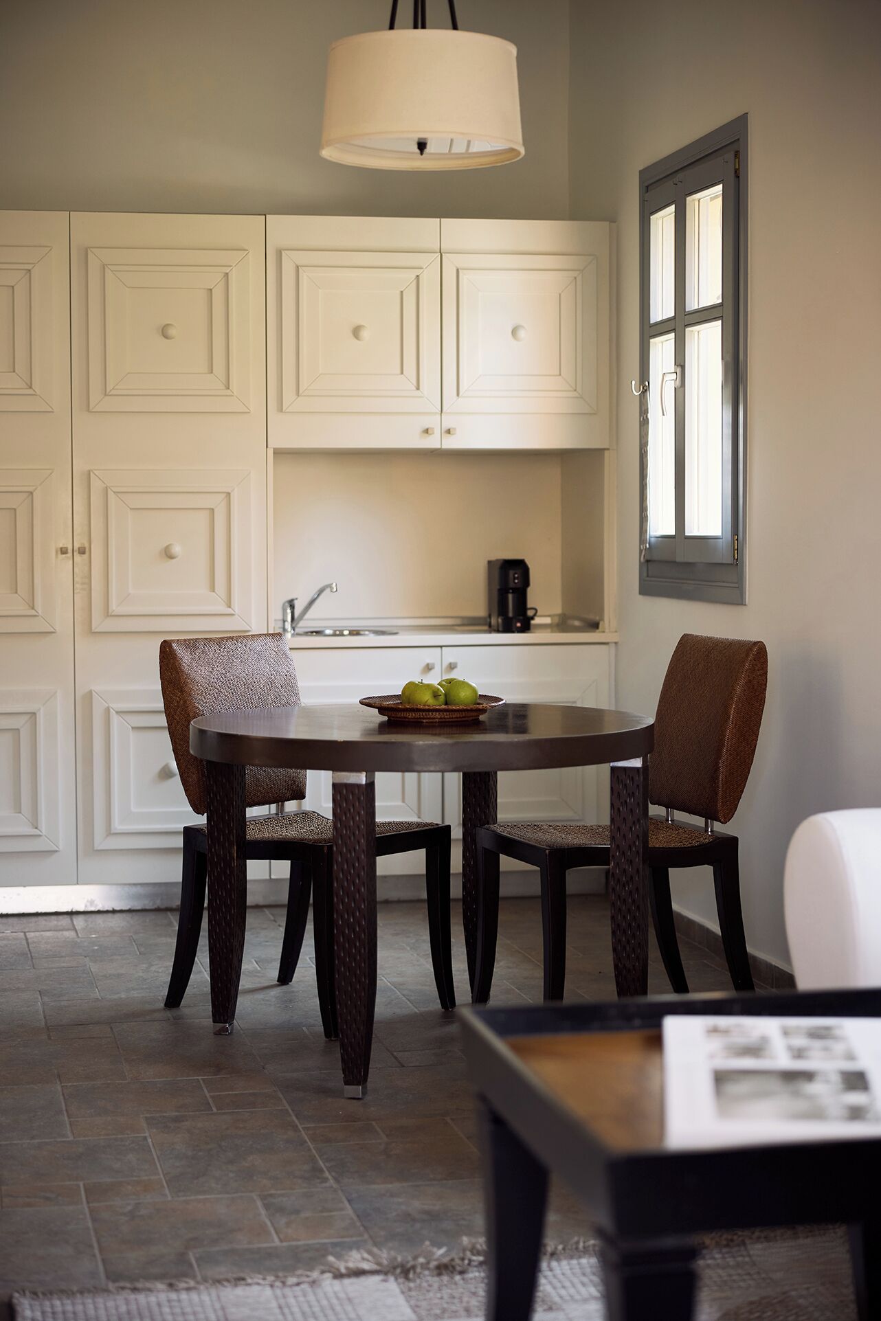 A dining area with a round table, two chairs, and a lamp above.