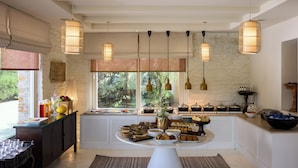 Une cuisine avec un buffet pour le petit-déjeuner, des suspensions décoratives et une vue sur les arbres à travers de grandes fenêtres.