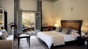 Une chambre avec un grand lit, une table de chevet, une chaise, une table et une vue sur l’extérieur grâce à une porte vitrée.
