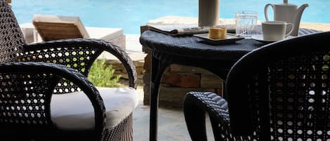 A poolside area with lounge chairs, a table with a vase and a teapot, and a view of the sea.
